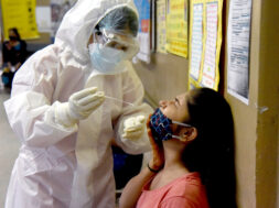 A health worker in (PPE) collects a sample using a swab from a girl
