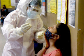 A health worker in (PPE) collects a sample using a swab from a girl