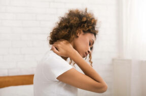 Woman suffering from neck pain, waking up in the morning, sitting on bed
