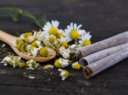 Chamomile flowers and herbal cigarettes on rustic table.